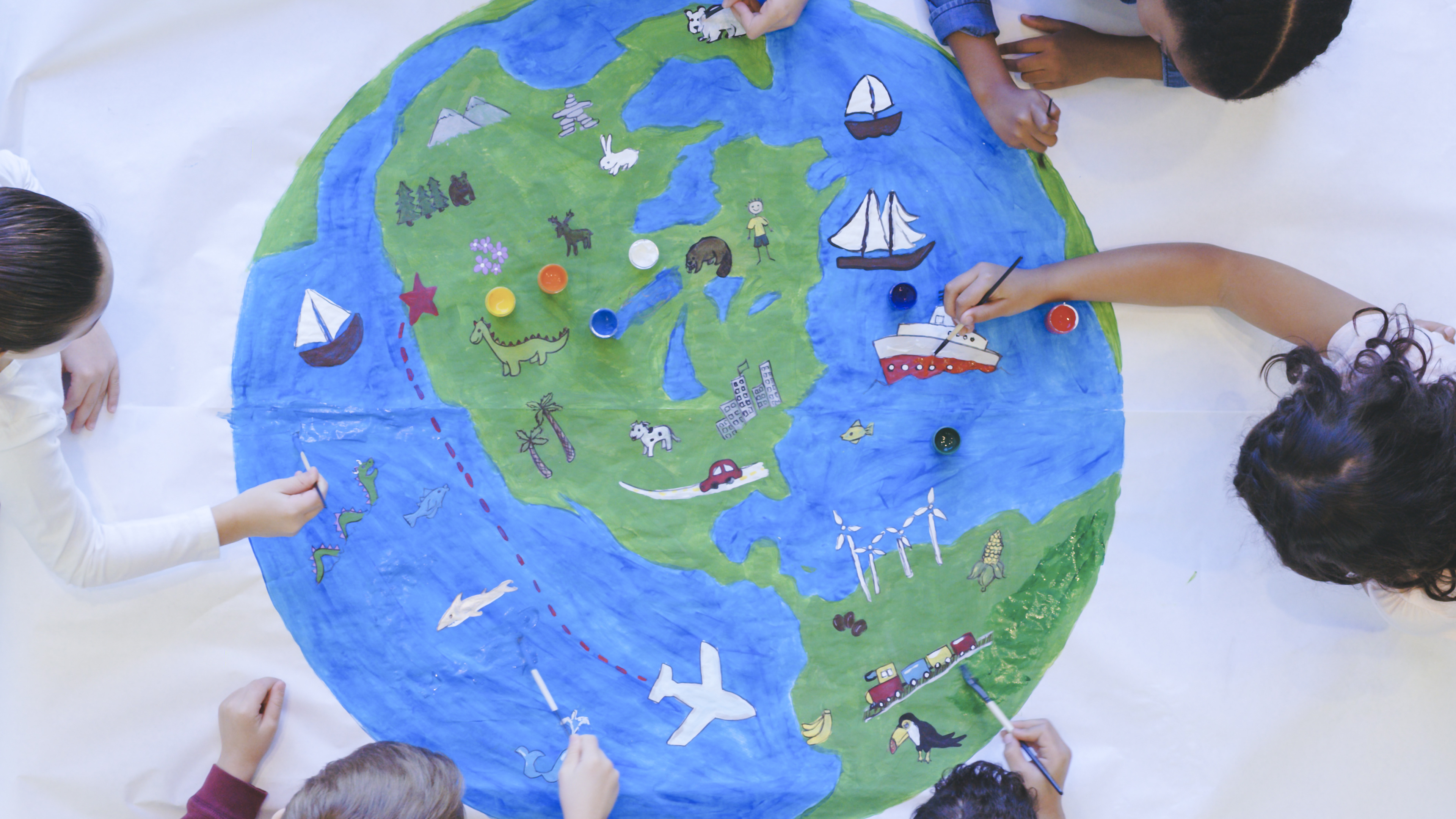 Das Bild zeigt auf dem Boden sitzende Kinder, die eine Weltkugel malen – 